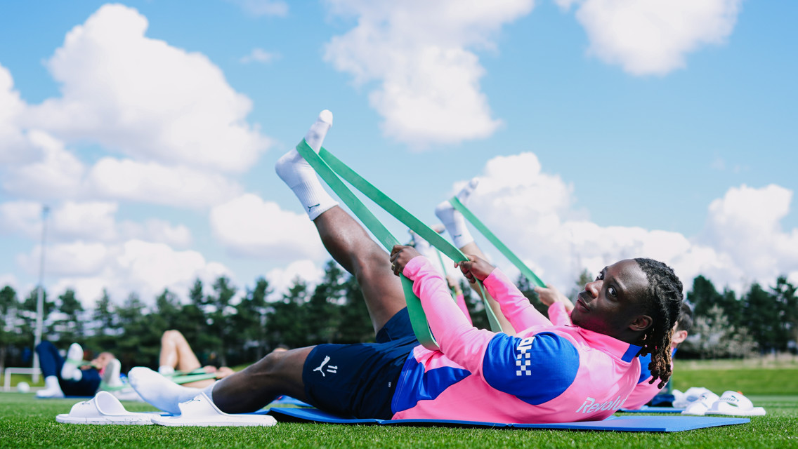 Athletes in pink jerseys use resistance bands for stretching exercises on a grassy field.