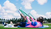 Athletes in pink jerseys use resistance bands for stretching exercises on a grassy field.