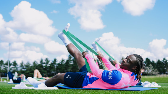 Athletes in pink jerseys use resistance bands for stretching exercises on a grassy field.
