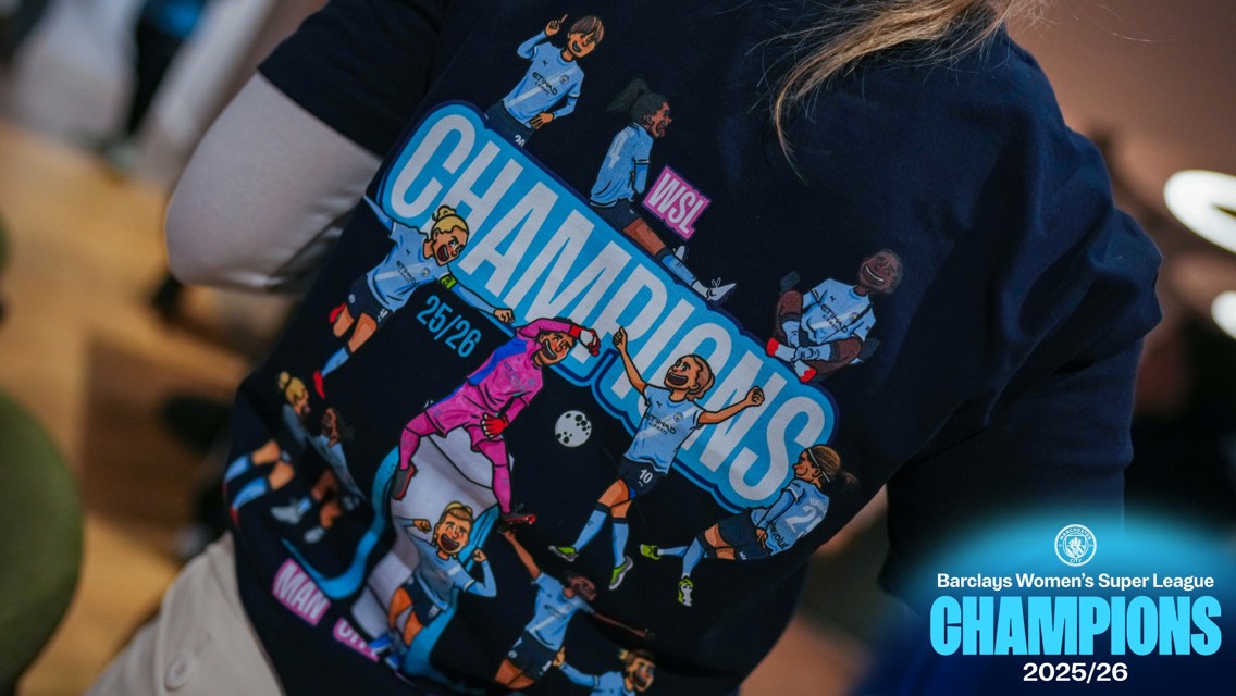 A close-up of a shirt featuring cartoon football players celebrating. It reads 'WSL Champions 25/26' and 'Barclays Women's Super League Champions 2025/26'.