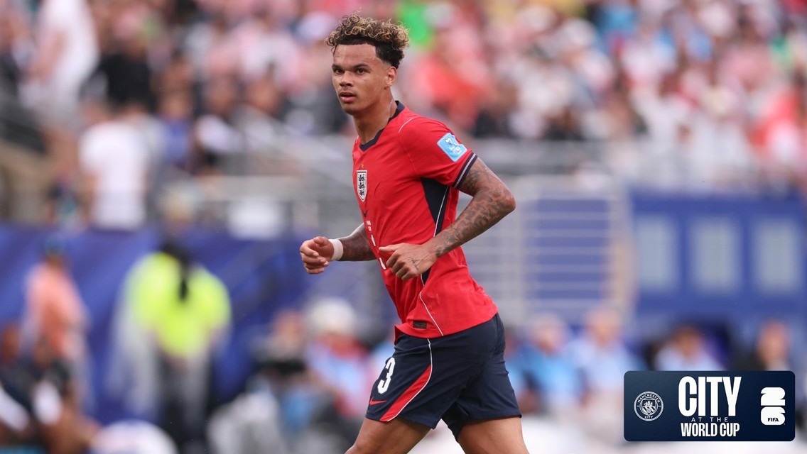 A football player wearing a red and navy jersey with number 3 is running on the field. The background shows a blurred crowd, and there's a CITY AT THE WORLD CUP logo.