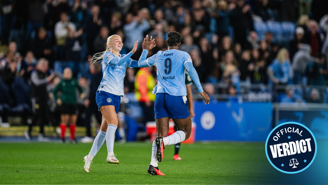 Two Manchester City women players celebrating during a football match, wearing light blue jerseys, with a crowd in the background.