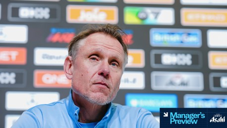 A person in a blue shirt at a press conference with a 'Manager's Preview' overlay. Background features multiple sponsor logos including Joie and British Gas. The face is obscured.