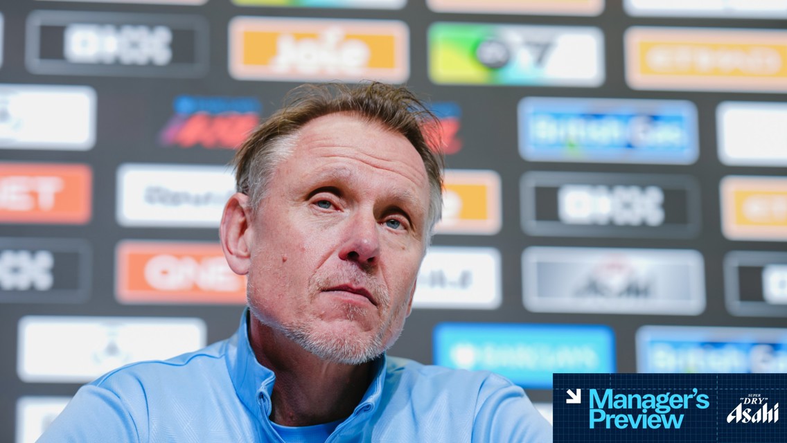 A person in a blue shirt at a press conference with a 'Manager's Preview' overlay. Background features multiple sponsor logos including Joie and British Gas. The face is obscured.