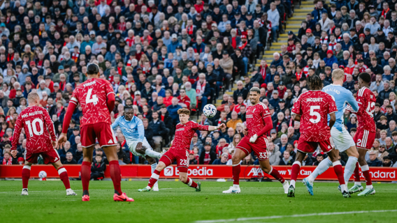 Soccer players in red and blue jerseys during a match, surrounded by spectators.