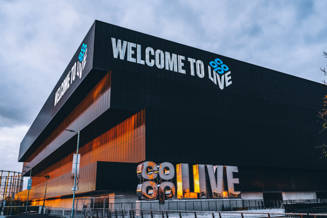 A modern black building with the text 'Welcome to Co-op Live' on the facade against a cloudy sky.