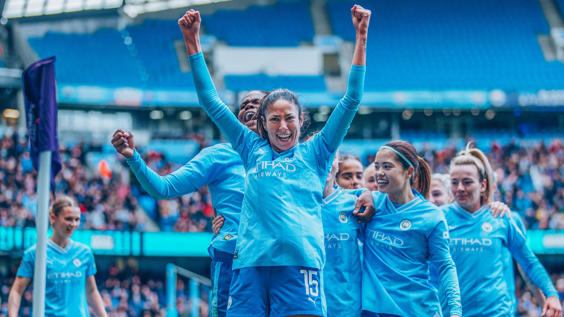Manchester City Women's team players celebrating on the field in blue jerseys after a goal.