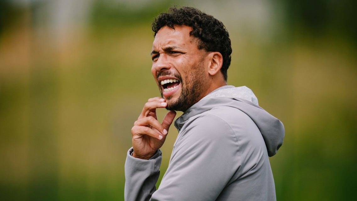 A person wearing a gray hoodie is outdoors, appearing to be shouting or giving instructions.