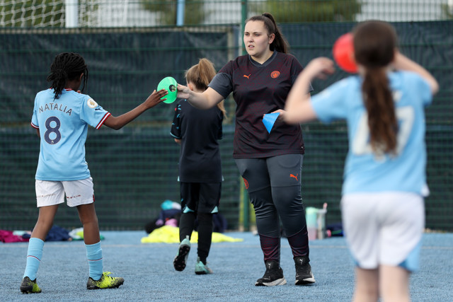 Young girls training session, one girl handing a marker cone to a coach.