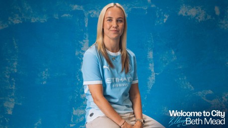 A person wearing a Manchester City football kit is seated against a textured blue background. Text reads 'Welcome to City Beth Mead.'