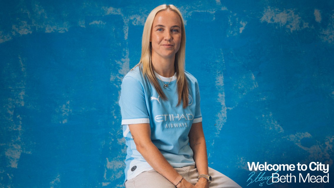 A person wearing a Manchester City football kit is seated against a textured blue background. Text reads 'Welcome to City Beth Mead.'