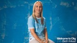 A person wearing a Manchester City football kit is seated against a textured blue background. Text reads 'Welcome to City Beth Mead.'