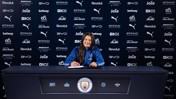 A person in a Manchester City jacket is signing a contract at a table with the club's logo. The background displays multiple sponsor logos.