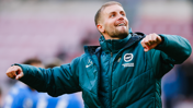 A person wearing a Brighton & Hove Albion jacket is celebrating, with arms raised and a joyful expression.