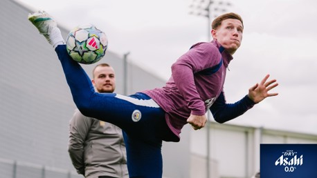 A soccer player in Manchester City training gear performing a high kick, attempting to control the ball during a practice session.