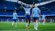 Manchester City women's soccer team celebrating a goal at the Etihad Stadium. Players wearing blue kits with numbers 25 and 11 visible.