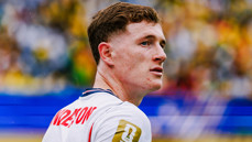 A soccer player wearing a white jersey with text on the back and a FIFA patch on the shoulder looking to the side during a match.