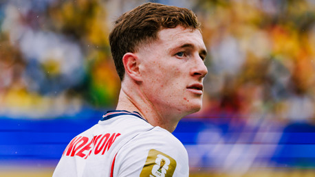 A soccer player wearing a white jersey with text on the back and a FIFA patch on the shoulder looking to the side during a match.