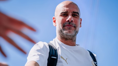 A man wearing a white Puma shirt and a black backpack extends his hand against a clear blue sky.