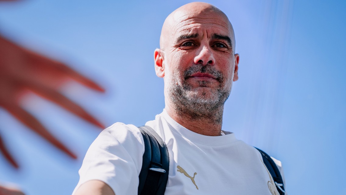 A man wearing a white Puma shirt and a black backpack extends his hand against a clear blue sky.