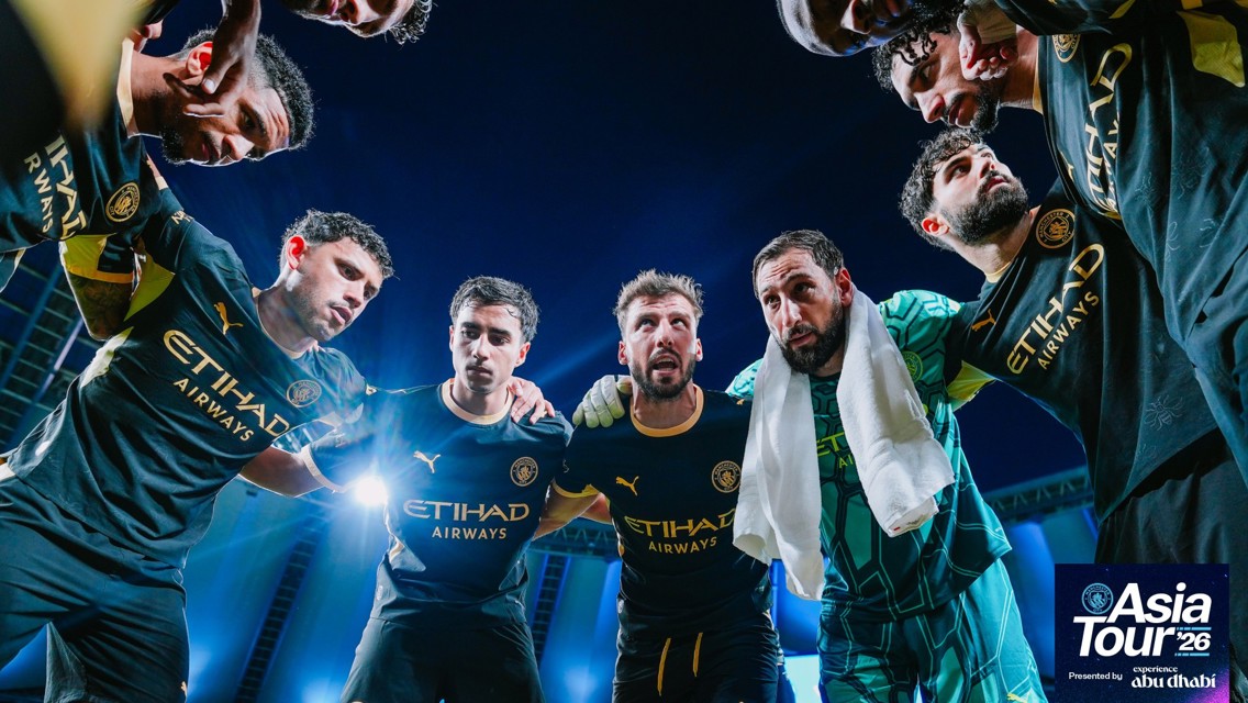 Players in Manchester City jerseys huddling with 'Asia Tour '26' branding. The jerseys display the Etihad Airways logo.