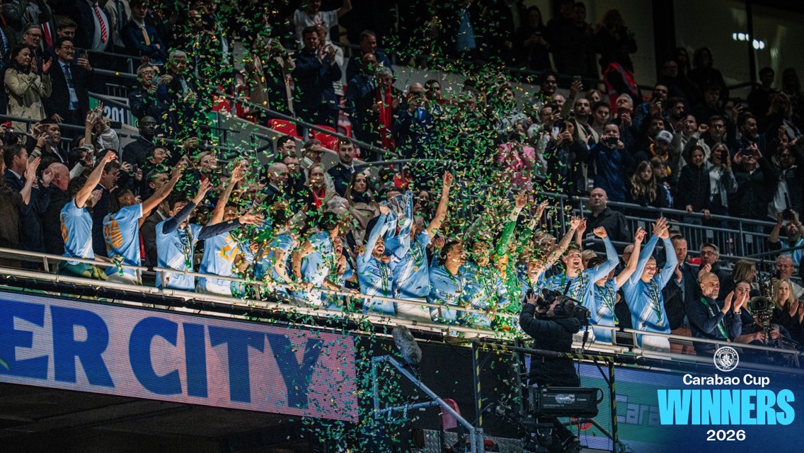 Football team celebrating with confetti after winning the Carabao Cup 2026. Players wearing blue shirts holding the trophy. Crowd cheering in stands.