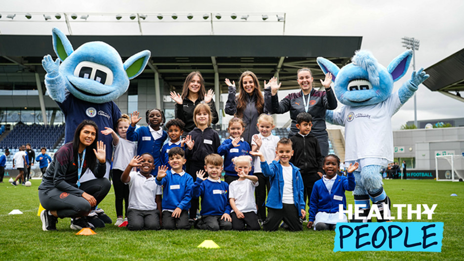 Group photo of children and Manchester City mascots Moonchester and Moonbeam during a community event at a football field