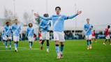 A Manchester City youth player with blurred face celebrates a goal with arms outstretched. Teammates in Manchester City kits are visible in the background.