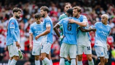 A group of Manchester City football players in light blue jerseys huddling on the field during a match.