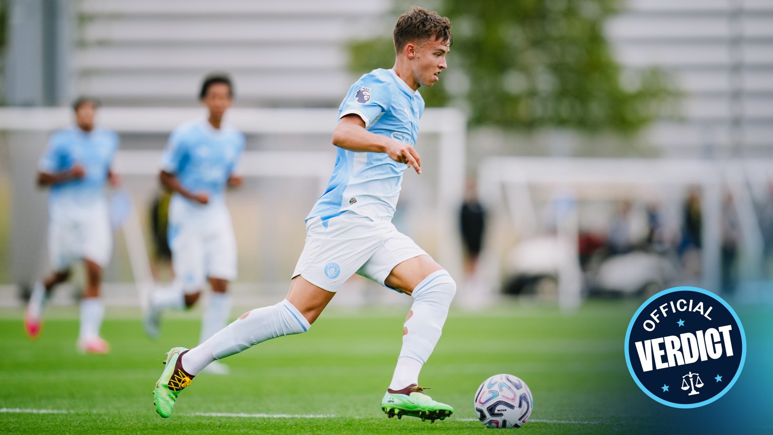 A soccer player in a light blue kit, running with the ball on a field during an intense match. Teammates blur in the background, focused on the game.