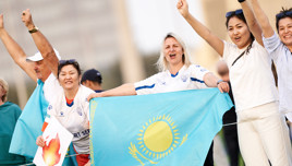Group of people cheering with a Kazakhstan flag, wearing various sports jerseys and showing excitement.