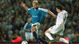Two football players in action during a match, one in a blue Manchester City jersey and the other in a white Leeds United jersey, near a football.