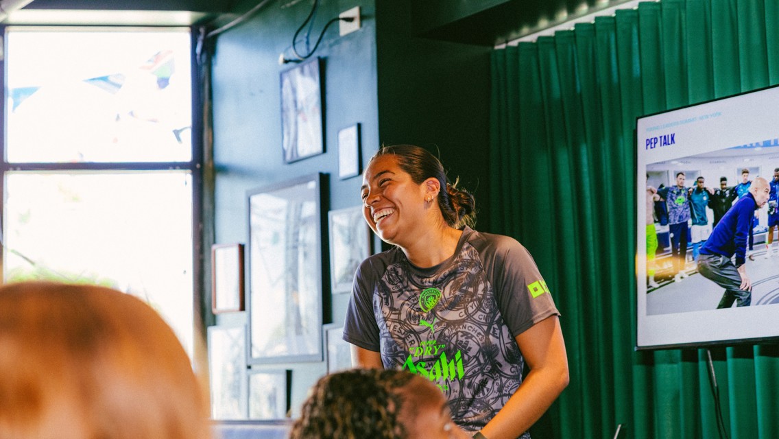A person wearing a Manchester City shirt is laughing during a presentation. There is a screen displaying a slide titled 'PEP TALK.'