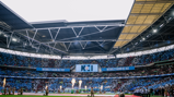 Wide view of Wembley Stadium with fireworks and a crowd. Banners with the Manchester City crest are visible.