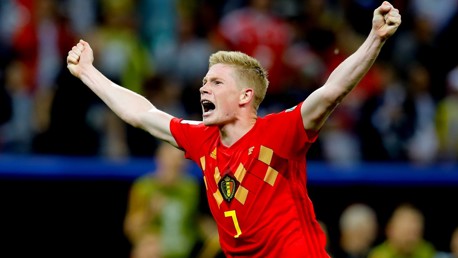 A football player in a red Belgium national team jersey with number 7 is celebrating with raised arms during a match.