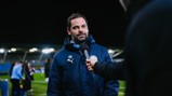 A person in a Manchester City jacket being interviewed with a microphone on a football field at night.