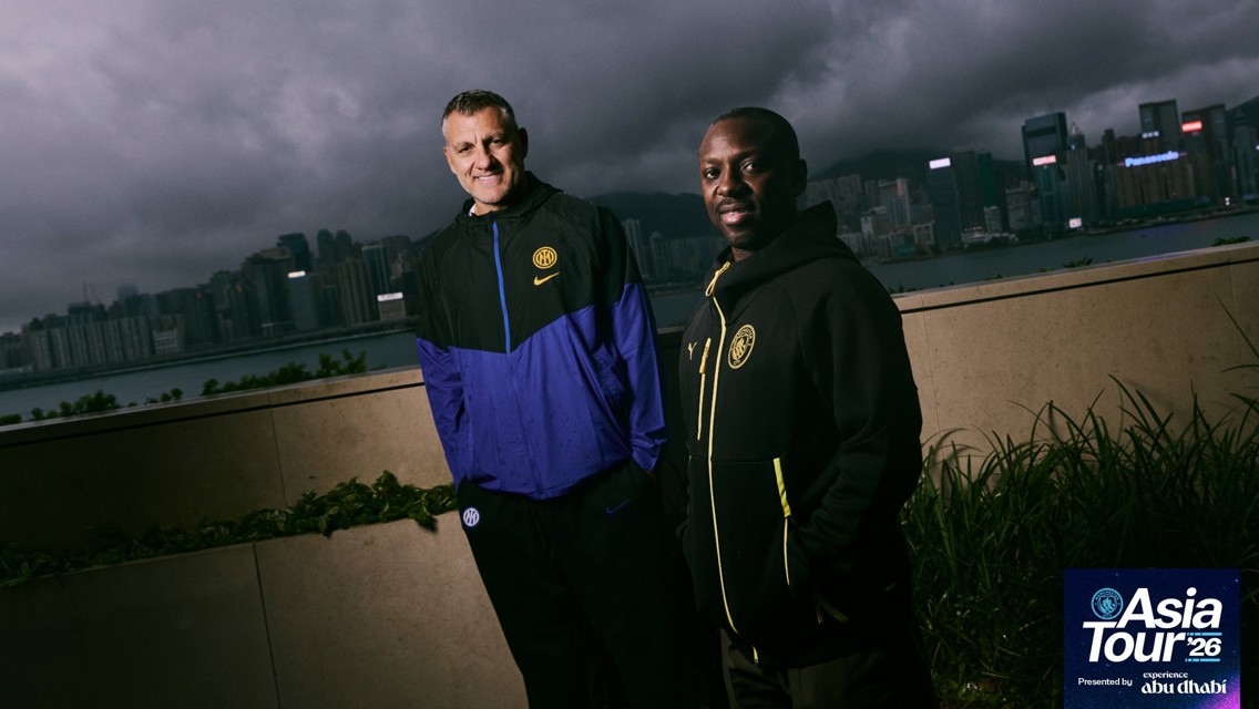 Two people in Inter football gear stand outdoors with a city skyline in the background, featuring 'Asia Tour '26'.