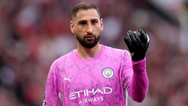 A goalkeeper wearing Manchester City's pink kit, featuring the club's logo and Etihad Airways sponsor. The player is wearing black gloves.