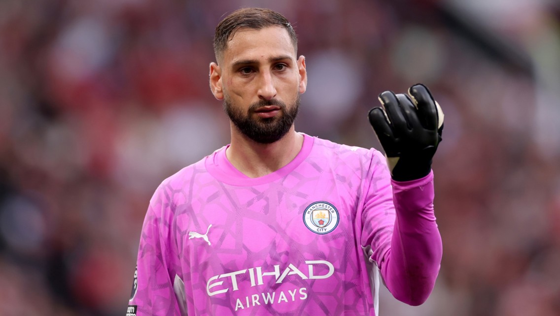 A goalkeeper wearing Manchester City's pink kit, featuring the club's logo and Etihad Airways sponsor. The player is wearing black gloves.