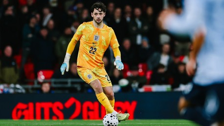 A football goalkeeper in a yellow kit with the number 22 prepares to pass the ball in a match.