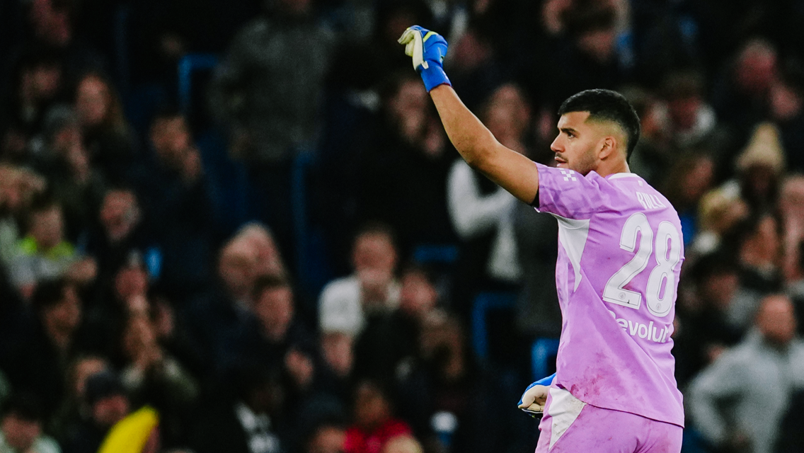 A football goalkeeper in a pink jersey with the number 28. He is raising his arm during a game, surrounded by a crowd.