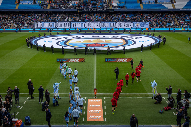 Manchester City Women's team and opposing team line up on the field at Etihad Stadium. Large Manchester City logo displayed; banner reads 'The only football team to come from Manchester'.