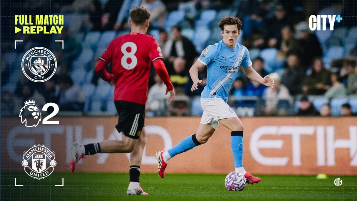 A soccer match between Manchester City and Manchester United. Player in light blue kit is dribbling past player in red. Score shows Manchester City 2 and Manchester United 0. Premier League branding visible.