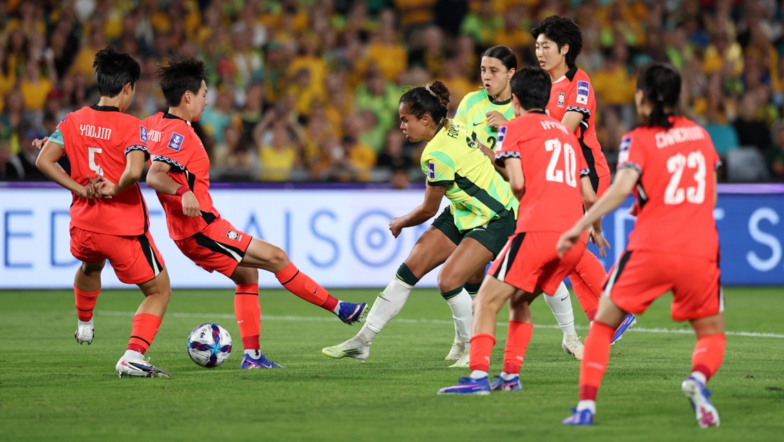 Soccer players wearing green and yellow and red kits are competing for the ball on the field during a match.