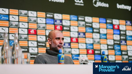 A person with a blurred face is seated in front of a mic and sponsor backdrop at a press conference. Bottles and sports drinks are on the table. Text reads 'Manager's Preview'.