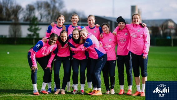 A group of women in pink training gear, likely a sports team, standing together on a grass field.