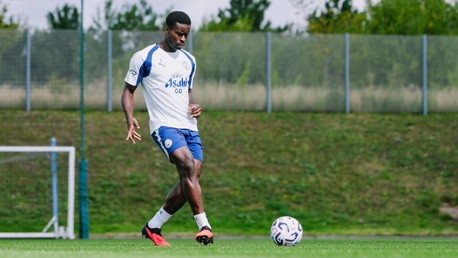 A soccer player in a white and blue Manchester City training kit is practicing with a ball on a grassy field.
