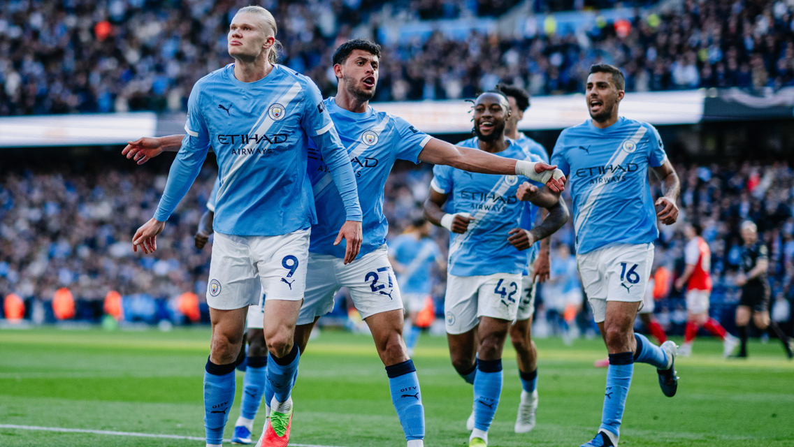 Players in Manchester City jerseys celebrate a goal on the field during a match.