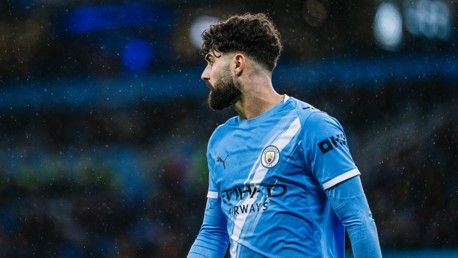 A Manchester City player in a blue and white striped jersey during a match in the rain.