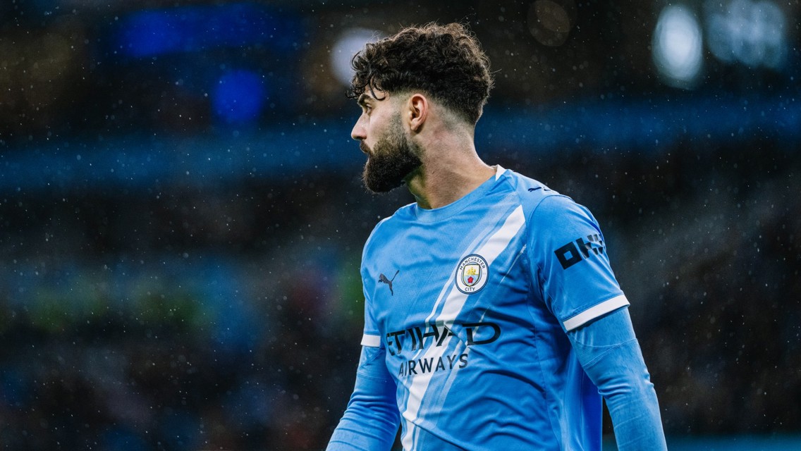 A Manchester City player in a blue and white striped jersey during a match in the rain.